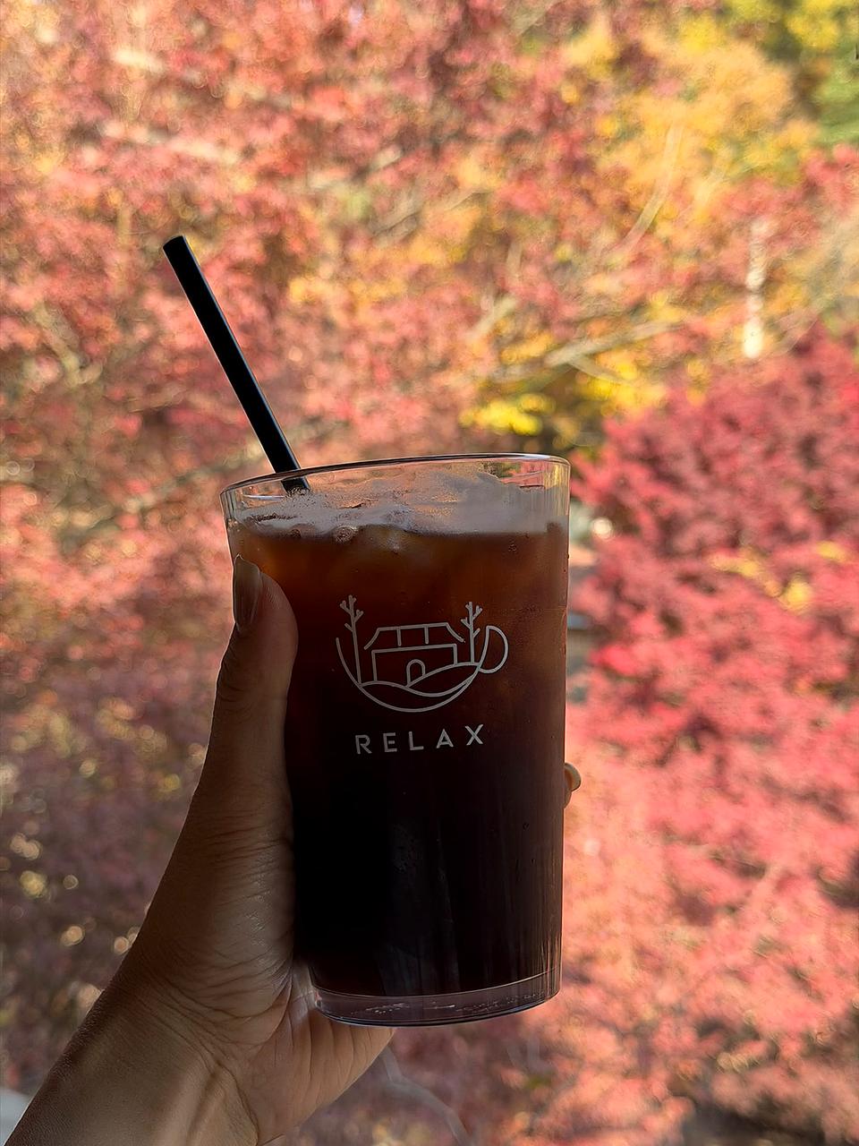 手持 RELAX 饮品与窗外红叶
