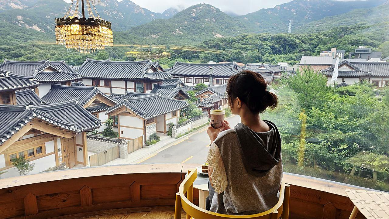 Enjoying a drink by the window overlooking Eunpyeong Hanok Village and the mountains